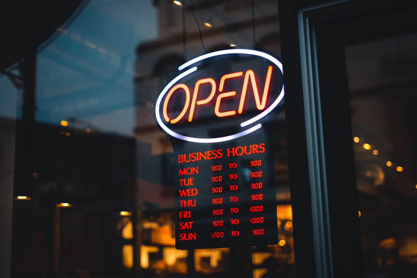 Neonfényes OPEN felirat és nyitvatartási tábla egy üzlet kirakatában este