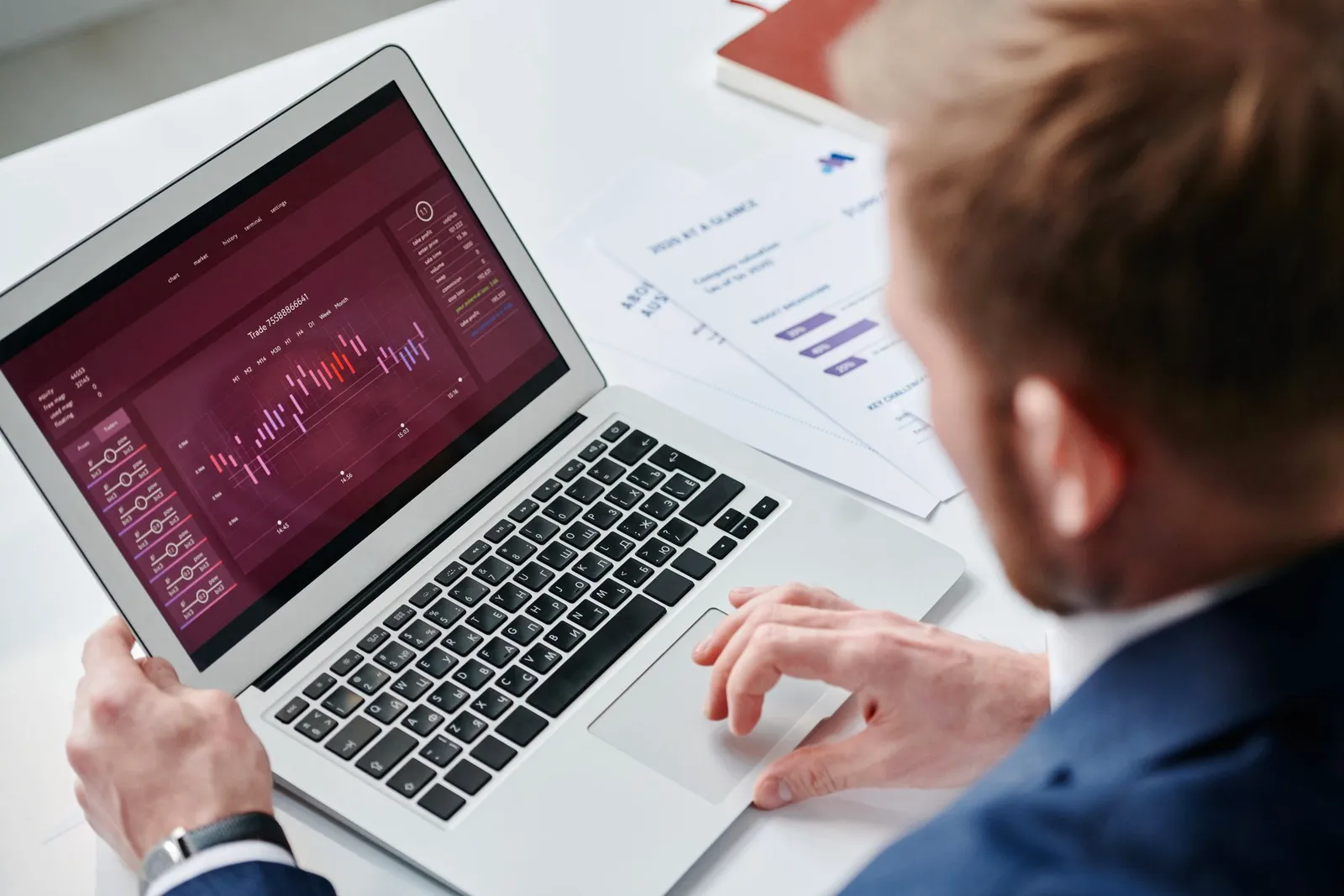 Férfi laptopon lila színű webanalitikai műszerfalat néz, mellette kinyomtatott jelentések